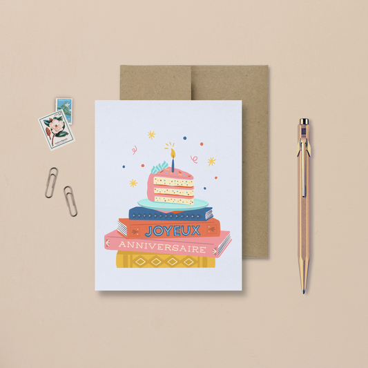 carte de souhait avec une illustration colorée d'une pile de livres et un gâteau d'anniversaire